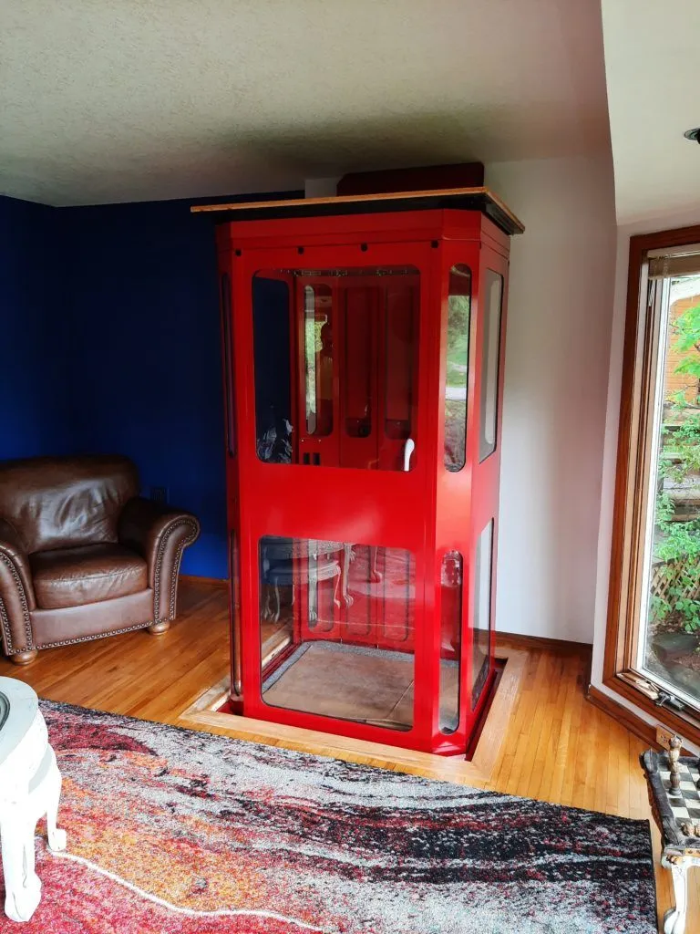 A customized red shaftless home elevator, also known as a through-the-floor elevator, takes up little space on the second story of a home.