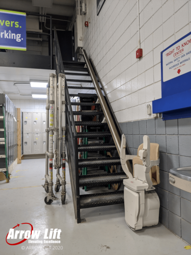 Commercial stair lift parked at base of stairs in warehouse - Arrow Lift 2020