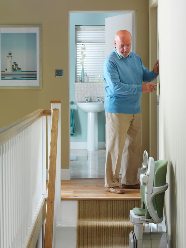 Man at the top of staircase operating a stair lift.