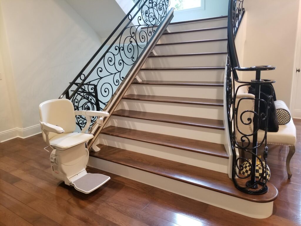 stairlift at the bottom of a stair case with an intricate iron railing