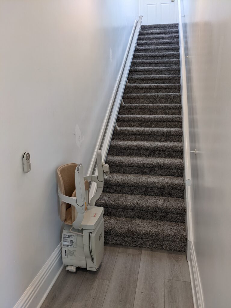 Straight stair lift with chair at the bottom landing in folded position