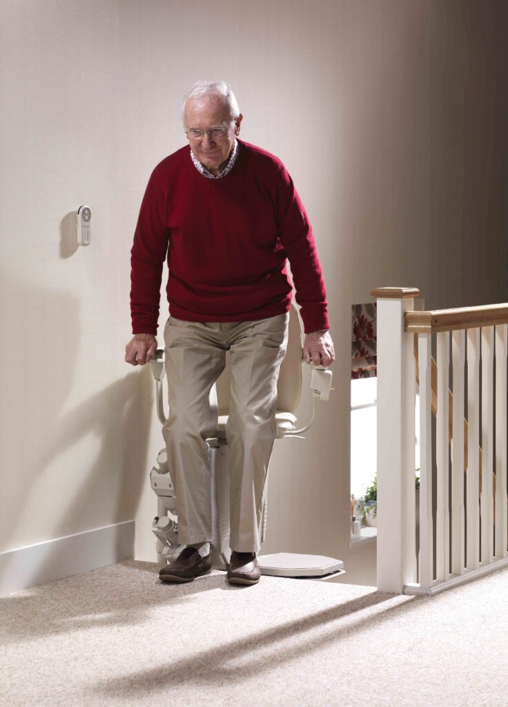 Man getting out of a stair lift at the top landing with the chair pivoted