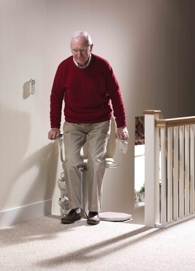 Man getting out of a stair lift at the top landing with the chair pivoted