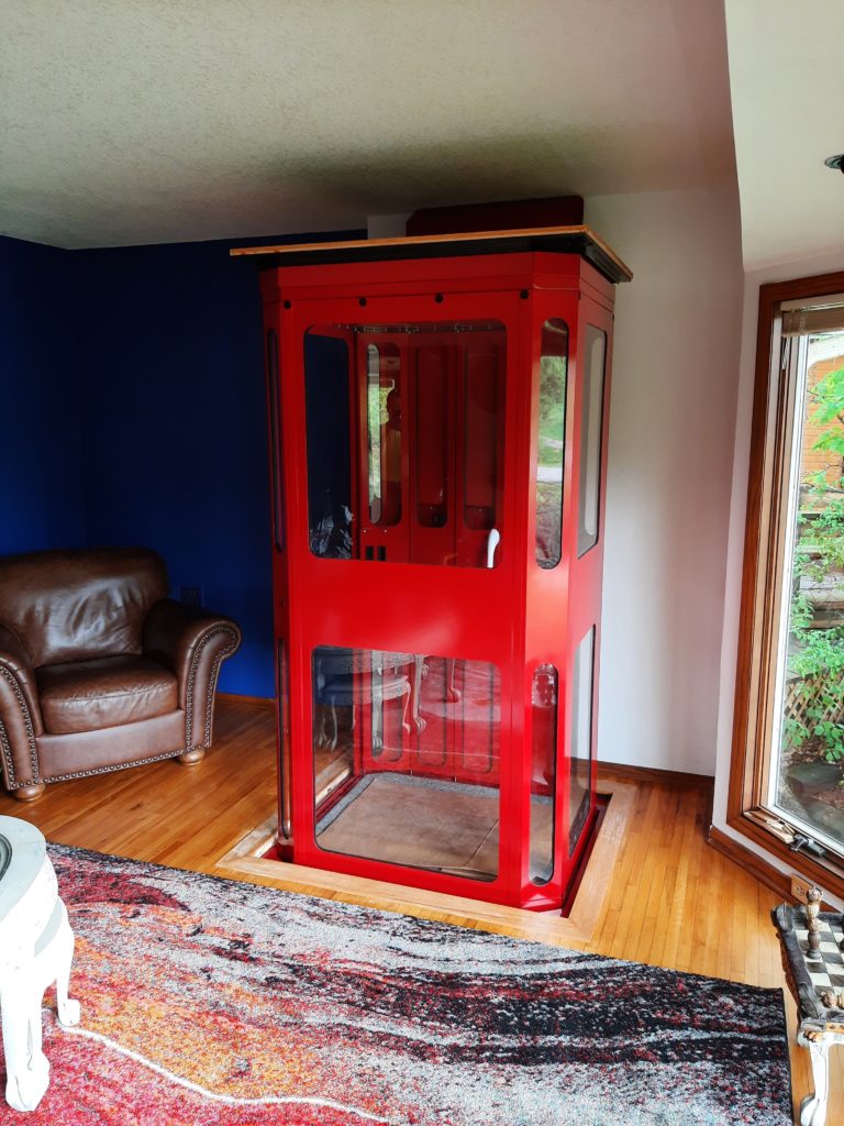 A customized red shaftless home elevator, also known as a through-the-floor elevator, takes up little space on the second story of a home.