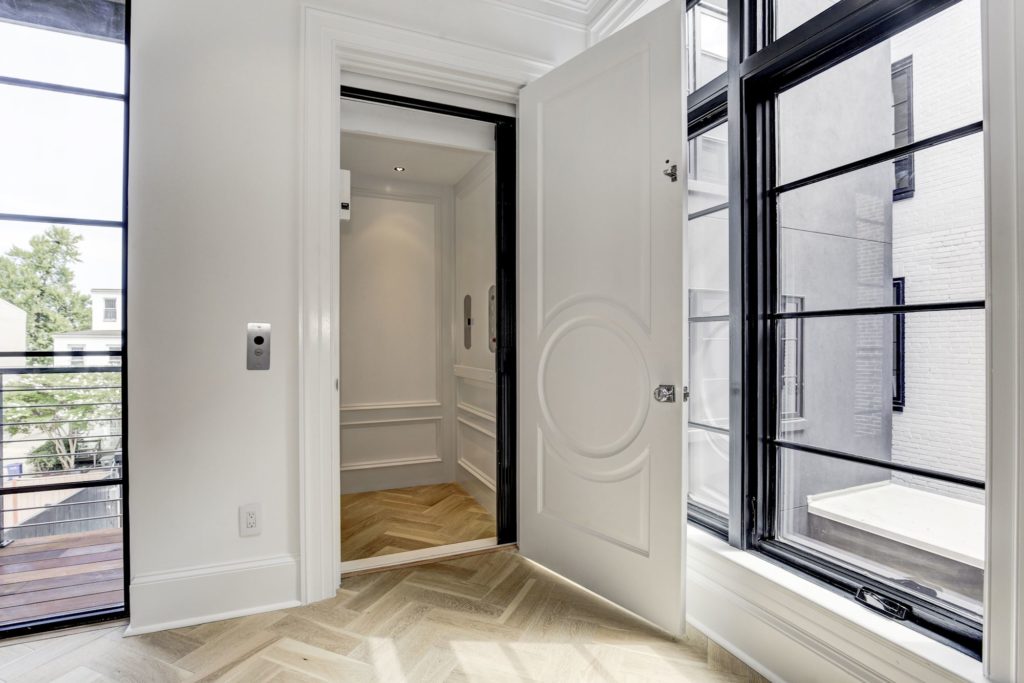 A white home elevator with crown molding and herringbone patterned wood floor, custom designed to match its surroundings and add value to the home.