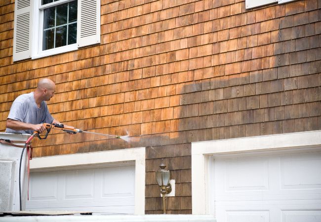 Home exterior with person using a power wash machine to clean siding. 