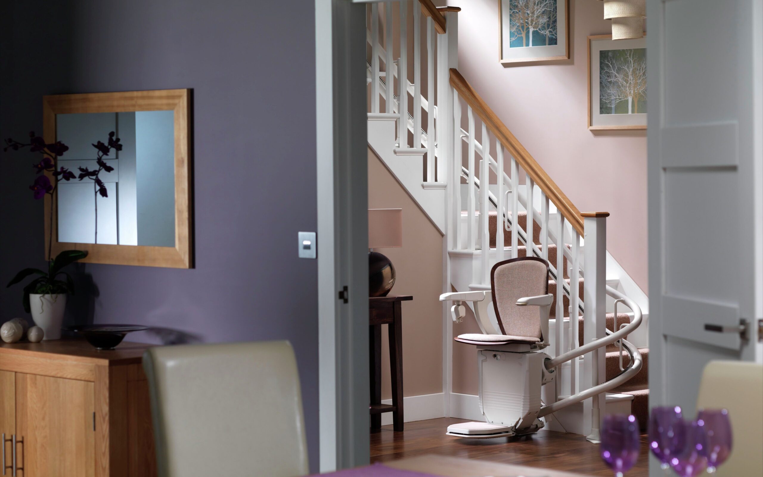 Image of curved stair lift parked at the base of staircase. Seen through an open doorway. 