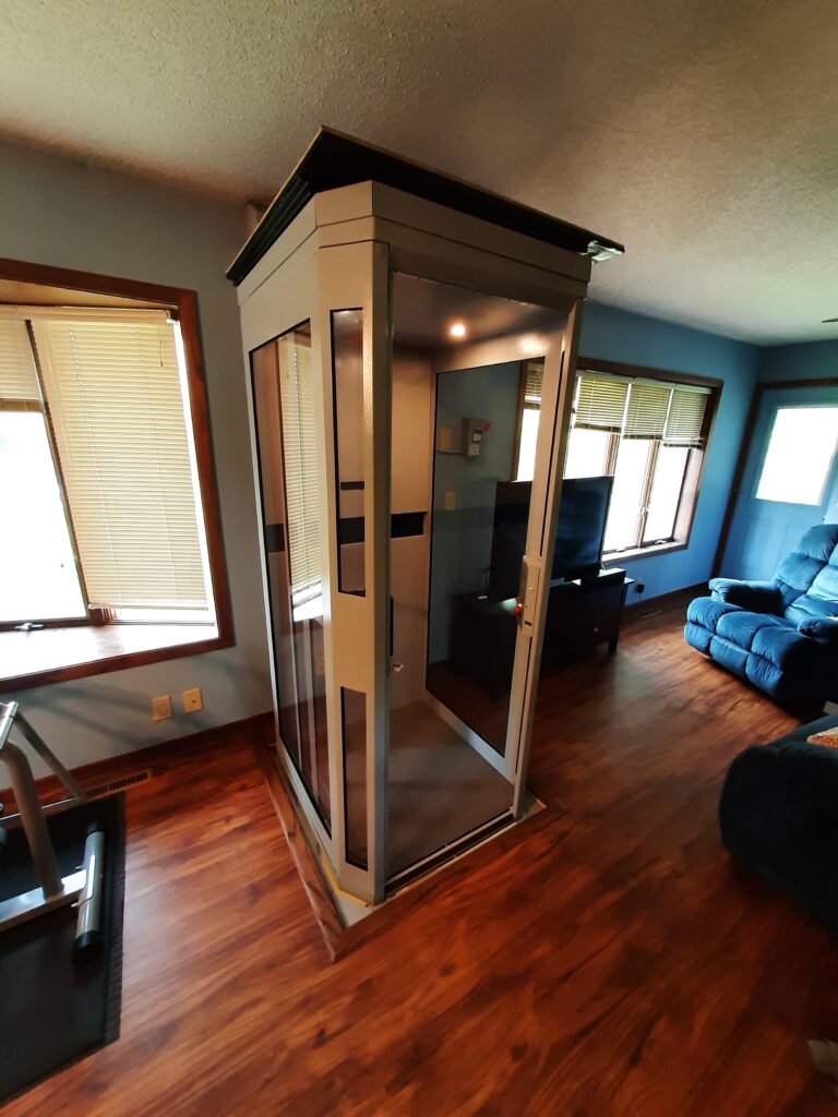 Shaftless Home Elevator at top landing in Living room of home. Door is open to elevator showing the front entry point.