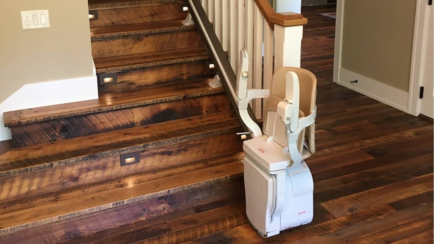 Stair lift parked at base of wood stairs, folded up for storage