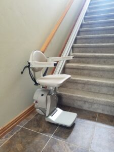 Used stair lift at the base of staircase with arms, chair and foot rest in the down position.