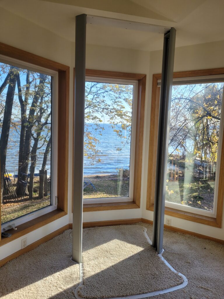 Residential through-floor home elevator lift track installation in a lakefront home with panoramic windows and natural light
