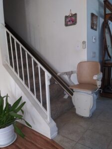 Stair lift at base of a carpeted staircase with chair and arms down.