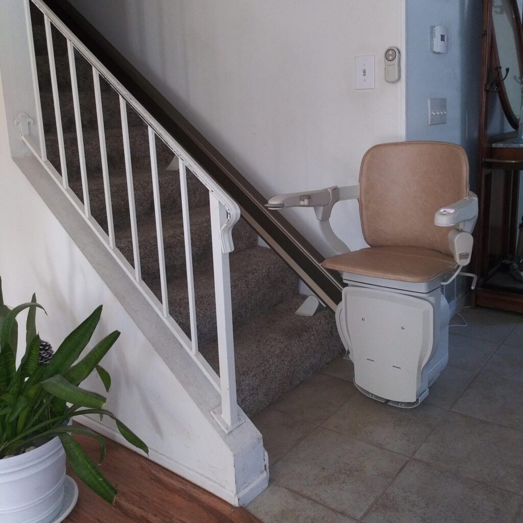 Stair lift at base of a carpeted staircase with chair and arms down.