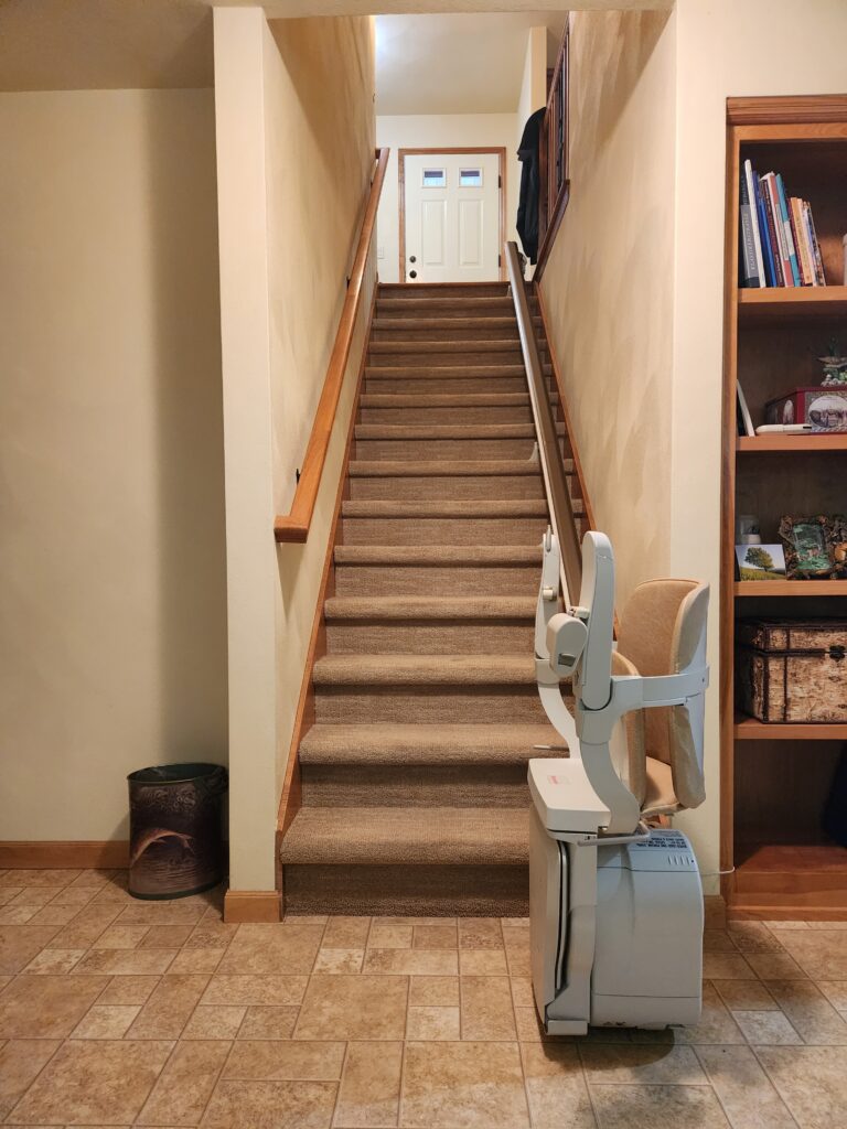 A stairway leading from the lower level of a home to the upper floor is affixed with a stair lift chair on a rail. 