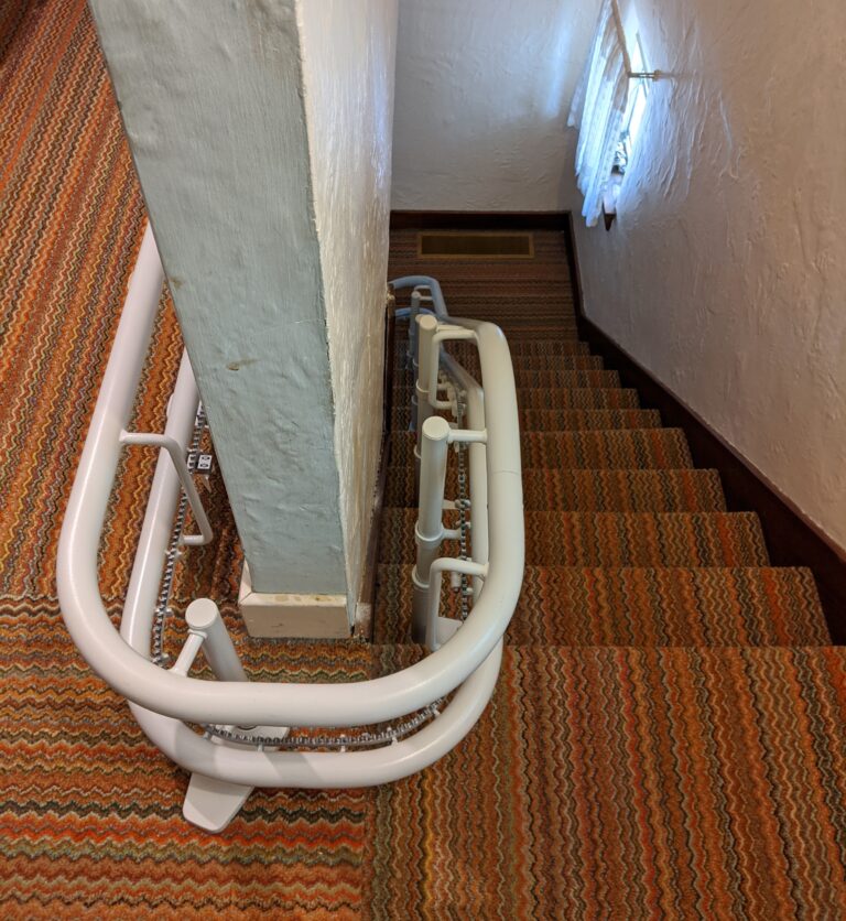 Curved stair lift rail showing rail attaching to stair treads and floor and curving around a wall