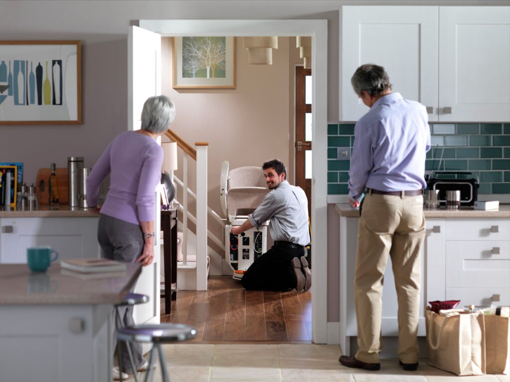 homeowners watch a smiling stair lift technician install their new stair lift chair