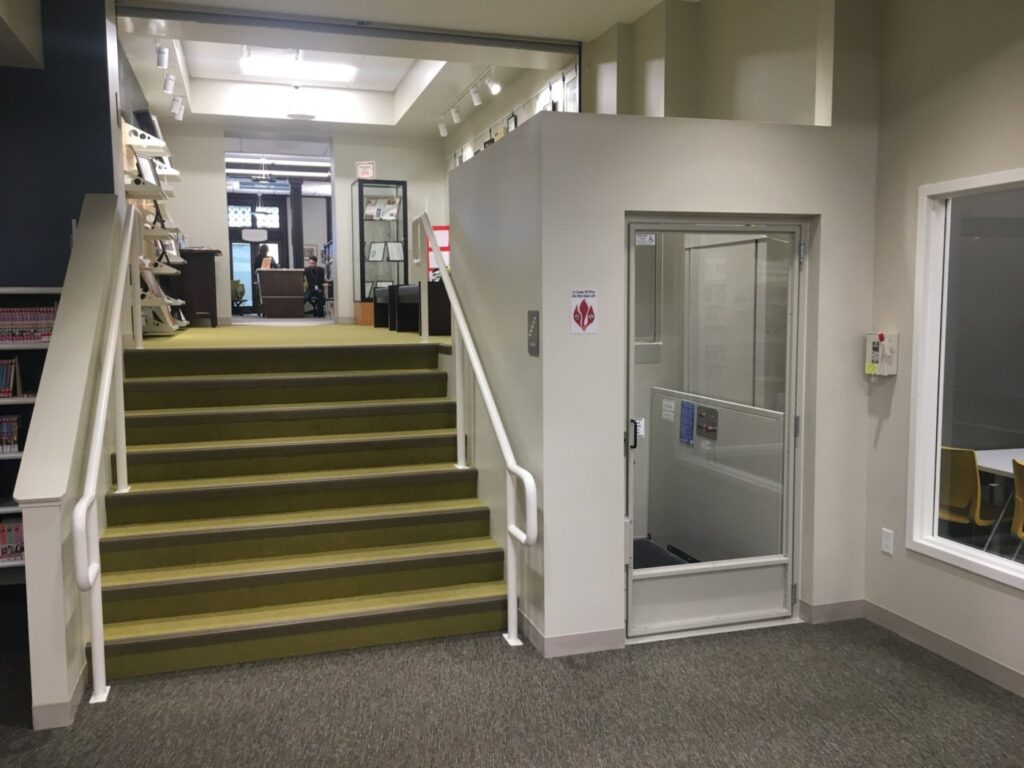 vertical platform lift in a small shaftway  beside the stairs in a library
